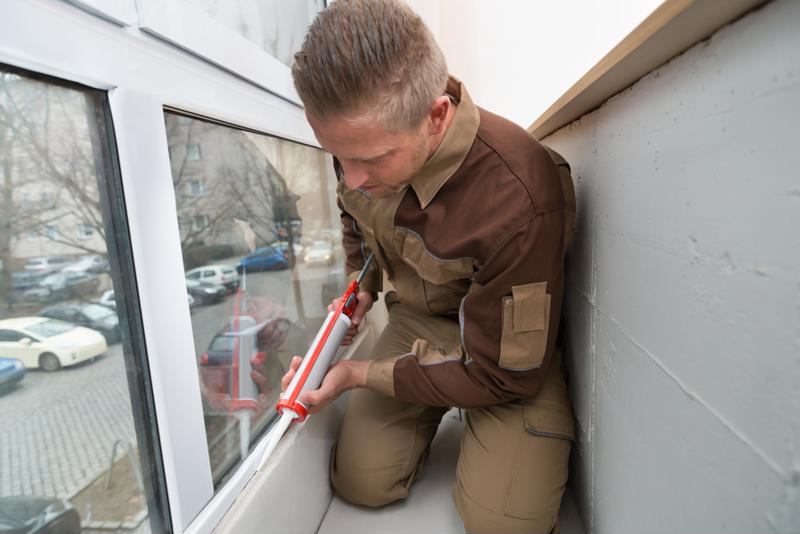 A man inserts caulking into a window sill.